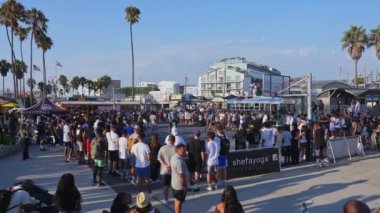 Venedik plaj kaykay parkında canlı bir kalabalık toplanıyor, palmiye ağaçları, açık bir gökyüzü ve Los Angeles, Kaliforniya 'daki ikonik Venedik tabelası.