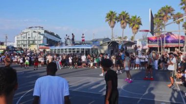 Venedik Sahili, Los Angeles 'ta canlı bir basketbol maçı var. Arka planda büyük bir kalabalık, palmiye ağaçları ve renkli duvar resimleri var..