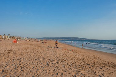 Los Angeles 'taki Venedik Plajı' nda kumlu sahillerde, sahile bakan binalarda ve açık mavi gökyüzünün altında uzak bir tepede yaşayan insanlar var..