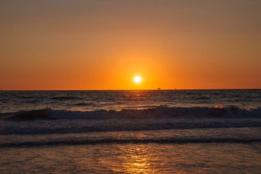 Los Angeles, Venice Beach 'te güneş ufuktan batıyor ve okyanus üzerinde turuncu bir parıltı oluşuyor. Sakin deniz manzarasına karşı bir tekne silueti görünür..