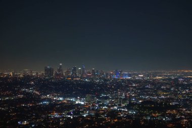 Los Angeles gökdelenleri karanlık bir gökyüzüne karşı parlayan gökdelenlerle gece görülür. Şehir ışıkları canlı bir duvar halısı oluşturarak şehir manzarasını vurguluyor..