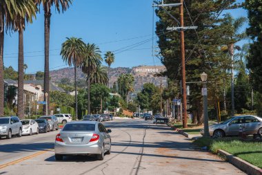 Bir Los Angeles caddesinde tepelerde uzun palmiye ağaçlarıyla kaplı Hollywood tabelası bulunur. Arabalar kenarlarda park halinde, gümüş renkli bir araba sürüyorlar..