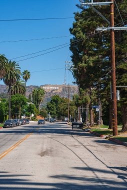 Arka planda, Los Angeles, Kaliforniya 'da sakin bir yerleşim yerindeki palmiye ağaçları ve elektrik direkleri tarafından çerçevelenmiş ikonik Hollywood tabelası görülüyor..
