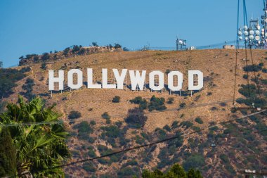 Hollywood tabelası Los Angeles, Kaliforniya 'nın kuru tepelerinde belirgin bir şekilde sergilenmektedir. İletişim kuleleri ve arka planda açık mavi bir gökyüzü vardır..
