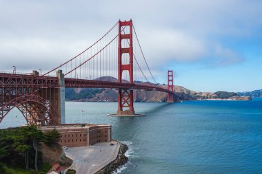 Golden Gate Köprüsü, üssünde Fort Point ile San Francisco Körfezi boyunca uzanır. Uluslararası Turuncu köprü mavi su ve Marin tepeleriyle çelişiyor.