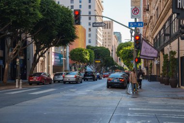 Arabalar, yayalar, ağaçlar ve açık mavi bir gökyüzünün altındaki sokak tabelalarıyla dolu tarihi İskenderiye Oteli manzarası.