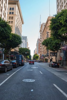 Los Angeles şehir merkezinde işlek bir sokak sahnesinde tarihi Orpheum Tiyatrosu tabelası, yüksek binalar, olgun ağaçlar ve güneşli bir günde açık mavi bir gökyüzü yer alıyor..