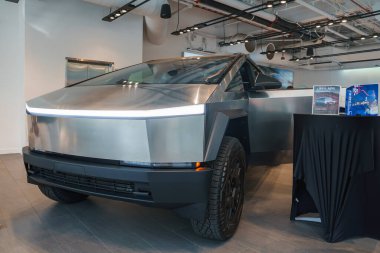 Paslanmaz çelik bir Tesla Siber Kamyonu, keskin hatlar ve metalik bir kaplamayla kapalı alanda sergileniyor. Galeride endüstriyel aydınlatma ve açıkta duran borular var..