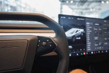 Görüntü bir Tesla aracının içini yakalıyor, iyi aydınlatılmış bir galeride direksiyonu ve merkezi dokunmatik ekranı siber kamyon arayüzü ile vurguluyor..