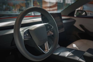 Modern bir arabanın içinde gösterişli bir direksiyon ve geniş bir dokunmatik ekran var. Günışığı lüks materyalleri vurguluyor, kentsel bir ortam öneriyor.