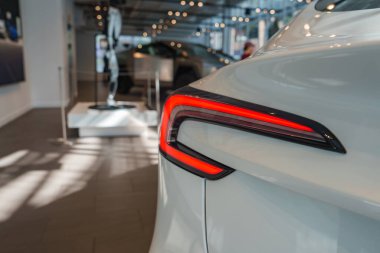 Parlak bir galeride eşsiz kırmızı stop lambaları olan parlak bir araba sergileniyor. Cilalı zemin ve çağdaş dekor aracın parlak kaplamasını güçlendirir.