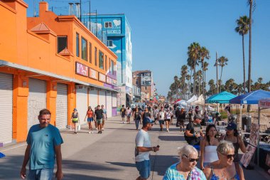 Los Angeles 'taki Venice Beach' te canlı turuncu ve mavi binalar, 'Aşk Dünyası' adlı duvar resmi ve açık mavi gökyüzü altında canlı bir kalabalık yer alıyor..