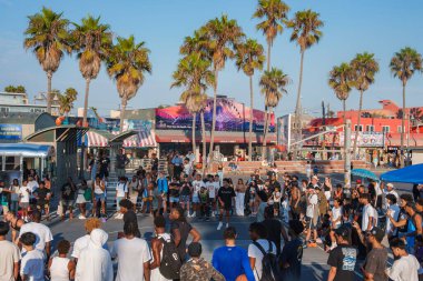 Güneşli bir günde Venedik Sahili, Los Angeles 'ta büyük bir kalabalık toplanıyor. Palmiye ağaçları, renkli duvar resimleri ve açık mavi gökyüzü altında mağazalar..