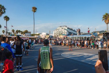 A vibrant scene at Venice Beach, Los Angeles, featuring a basketball game on an outdoor court. Tall palm trees and the bustling boardwalk are visible in the background. clipart