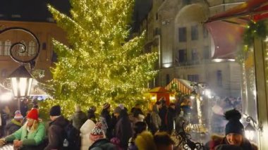 Riga Noel pazarında kalabalık bir ağaç, kalabalık kalabalık kalabalık, geleneksel tezgahlar ve tarihi binalar yer alıyor ve festival atmosferi yaratıyor..