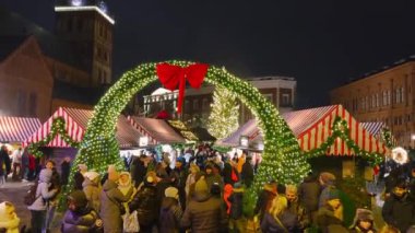 İnsanlar parlayan ışıklar, çizgili tezgahlar, yanan bir ağaç ve manzarası kilise kulesi olan tarihi binaların yer aldığı Riga Noel pazarını seviyorlar..