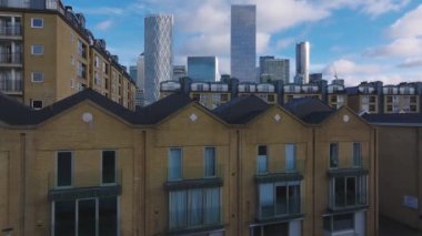 Londra 'nın Kanarya Rıhtımı' nın hava perspektifi, ikonik gökdelenler ve parçalı bulutlu gökyüzü altındaki yerleşim binaları.