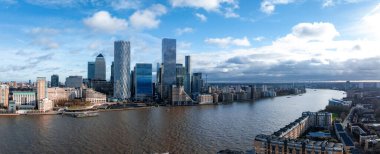 Londra 'daki Canary Wharf' ın hava perspektifi One Canada Square ve parçalı bulutlu gökyüzünün altındaki Thames nehri gibi modern gökdelenleri vurguluyor..