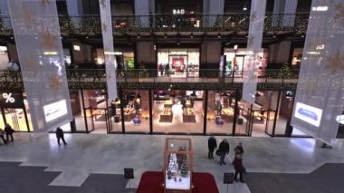 Battersea Elektrik Santrali 'nin iç kısımlarında Noel süsleri, cam mağazalar ve yüksek bir tavan yer alıyor. Alışveriş yapanlar Noel ağacı vitrininin önünden geçiyorlar..