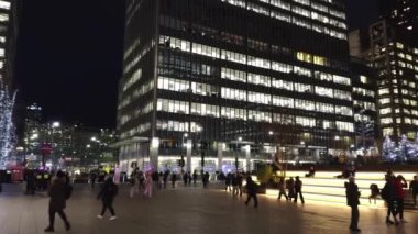 Canary Wharf 'ın ışıl ışıl gece hayatı aydınlık gökdelenler, hareketli yayalar ve gece gökyüzüne karşı belirgin bir Kanarya Rıhtımı işareti.