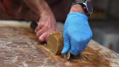 Bir insan spatula ve bıçak kullanarak bir kalıp karamel renkli şekerlemeyi bir mutfakta veya atölyede hijyene odaklanarak şekillendirir ve düzleştirir..