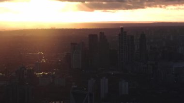 Günbatımında Londra siluetinde, tarihi ve çağdaş mimari sergilenen canlı renklere karşı siluetlenmiş Battersea Enerji İstasyonu ve modern gökdelenler yer almaktadır..