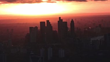 Güneş Londra 'nın üzerinde batıyor, ufuk çizgisine altın rengi yansıtıyor. Gökdelenler canlı gökyüzüne karşı siluetlendi. Aşağıda Thames Nehri görülebiliyor..