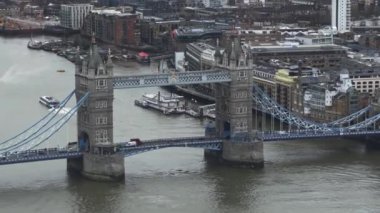 Tower Köprüsü 'nün ikonik kuleleri ve süspansiyonu Thames Nehri' ni kapsıyor ve bir tekne geçiyor. Londra 'nın çeşitli mimarisi bulutlu gökyüzünü çerçeveliyor.