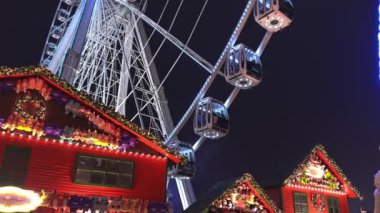 Hyde Park, Londra 'daki kış harikalar diyarı gece manzarası, büyük bir dönme dolap, şenlikli ışıklar, renkli gösteriler, ve hareketli tatil kalabalıkları.