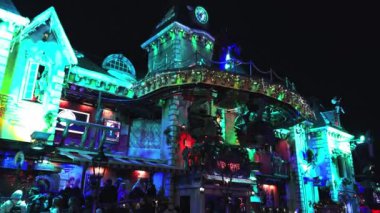 Londra 'daki Kış Harikalar Diyarı' nda, Noel atmosferinin keyfini çıkaran kalabalıkla çevrili, neşeli ışıklar ve dekorasyonlarla süslenmiş bir binanın olduğu canlı bir sahne..