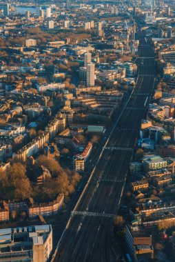 Londra 'nın havadan görünüşü, merkezi demiryolu hattı olan yoğun bir şehir manzarasını ortaya çıkarıyor. Şehir manzarası, yapraksız ağaçlar ve ikonik ufuk çizgisiyle sıcak ışıkla aydınlatılır..