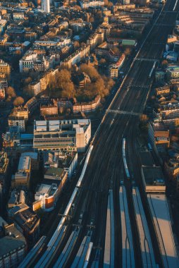 Londra 'nın şehir manzarasının demiryolu rayları, modern ve tarihi binalar ve sıcak, altın ışıkla aydınlatılmış yeşillik perspektifi.