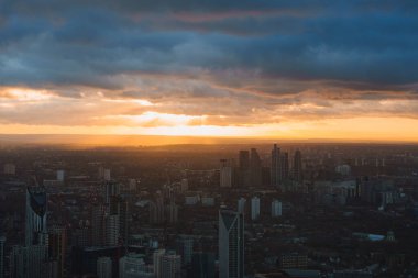 Londra 'nın günbatımında gökdelenler ve dramatik bulutlarla dolu gökdelenlerin ve modern binaların yer aldığı gökyüzü manzarası.