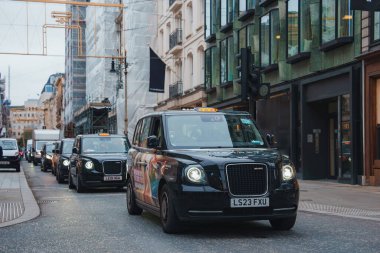 Londra 'nın hareketli caddesinde modern ve geleneksel mimarinin ortasında ikonik siyah taksiler yer alıyor. Noel süsleri sahneye şenlikli bir dokunuş ekler..