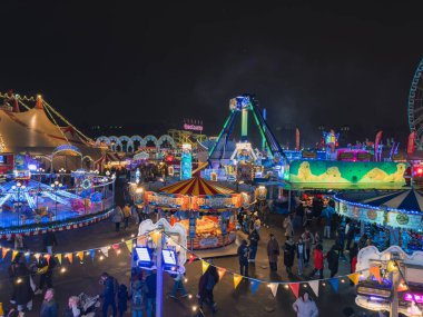 Londra 'daki Winter Wonderland' da hareketli bir gece sahnesi, büyük bir atlıkarınca, lunapark treni ve festival ışıklarının yer aldığı. Kalabalık canlı kış atmosferinin tadını çıkarıyor..