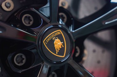 Lamborghini Revuelto tekerleğinin detaylı bir görüntüsü, parlak siyah arka planda simgesel altın boğa amblemi, parlak jantlar ve bijon fındıkları.