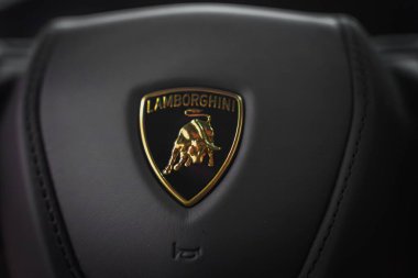 Görüntü Lamborghini ambleminin detaylı bir görüntüsünü yakalıyor, siyah bir kalkanda altın bir boğa, Revuelto direksiyon simidinin parlak yüzeyine karşı kurulmuş..