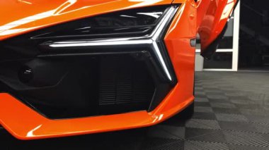 Video, Lamborghini Revuelto 'nun açısal tasarımını, canlı turuncu rengini ve makas kapıları olan modern bir galerinin farlarını yakalıyor..