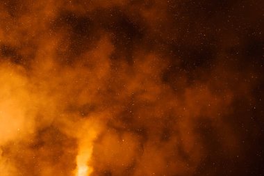 Orange smoke or dust swirls dramatically against a dark sky, illuminated by artificial light. Tiny specks resembling stars add a celestial quality. clipart