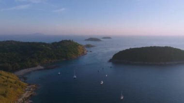 Uçurumda beyaz bir deniz feneri, yemyeşil tepeler, demirli yelkenliler ve uzak adaların bulunduğu Phuket Adası 'nın kıyı bölgesinin havadan görüntüsü..