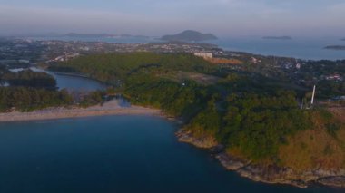 Phuket Adası 'nın havadan görünüşü, sakin bir sahil, yemyeşil tepeler, sakin bir mavi deniz, bir yelkenli, kentsel binalar ve uzak adaları gösteriyor..