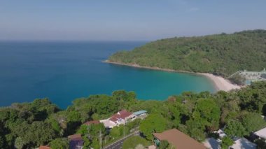 Tayland, Phuket Adası 'nın hava manzarası, yemyeşil bitki örtüsü, durgun mavi okyanus, açık gökyüzü ve kıyı şeridi yakınlarındaki binalar.