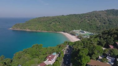 Turkuaz suları, beyaz kumu, yeşil tepeleri, bir tatil köyü, dolambaçlı bir yolu ve Tayland 'ın Phuket kentindeki uzak bir alanı olan sakin bir sahil manzarası..