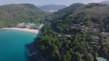Tayland 'daki Phuket Adası' nın havadan görünüşü turkuaz körfez, kumlu sahil, kayalık kıyı şeridi, yemyeşil tepeler ve uzak kentsel yapılar gösteriyor..