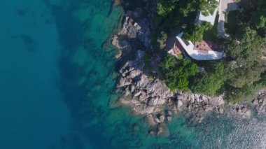 Tayland, Phuket Adası 'nın havadan görünüşü, kayalık bir sahil şeridi, yemyeşil bitki örtüsü, berrak turkuaz suları ve sualtı kaya oluşumlarını gösteriyor..