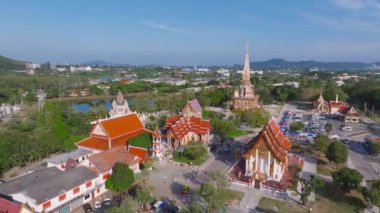 Phuket, Tayland 'daki Wat Chalong tapınağının havadan görünüşü, altın kulesi, yemyeşil bahçesi, park alanı, bir pazar, bir göl ve uzak tepeler..