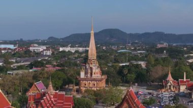 Phuket, Tayland 'daki Wat Chalong' un havadan görünüşü, altın kulesini, kırmızı çatılarını, yemyeşil çatılarını, uzak tepelerini ve kıyı şeridini gösteriyor..