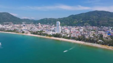 Tayland 'daki Phuket Adası' nın havadan görünüşü kumlu bir sahil, turkuaz sular, tekneli rıhtımlar, yemyeşil tepeler ve kentsel tatil köyleri gösteriyor..