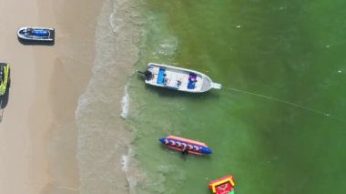 Tayland 'da berrak yeşil sular, uzun kuyruklu bir tekne, daha küçük bir tekne ve kıyı boyunca yürüyen iki kişinin bulunduğu sakin bir Phuket sahili..