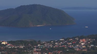 Tayland 'ın Phuket Adası' nın hava perspektifi, kıyı kasabasını, yemyeşil yeşillikleri, yuvarlanan tepeleri ve tekne ve adalarla Andaman Denizi 'ni gösteriyor..